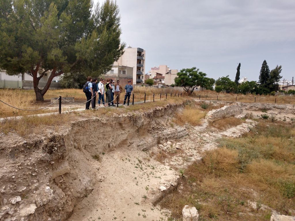 A view across an archaeological site, including a large stone wall, with the group in the distance.