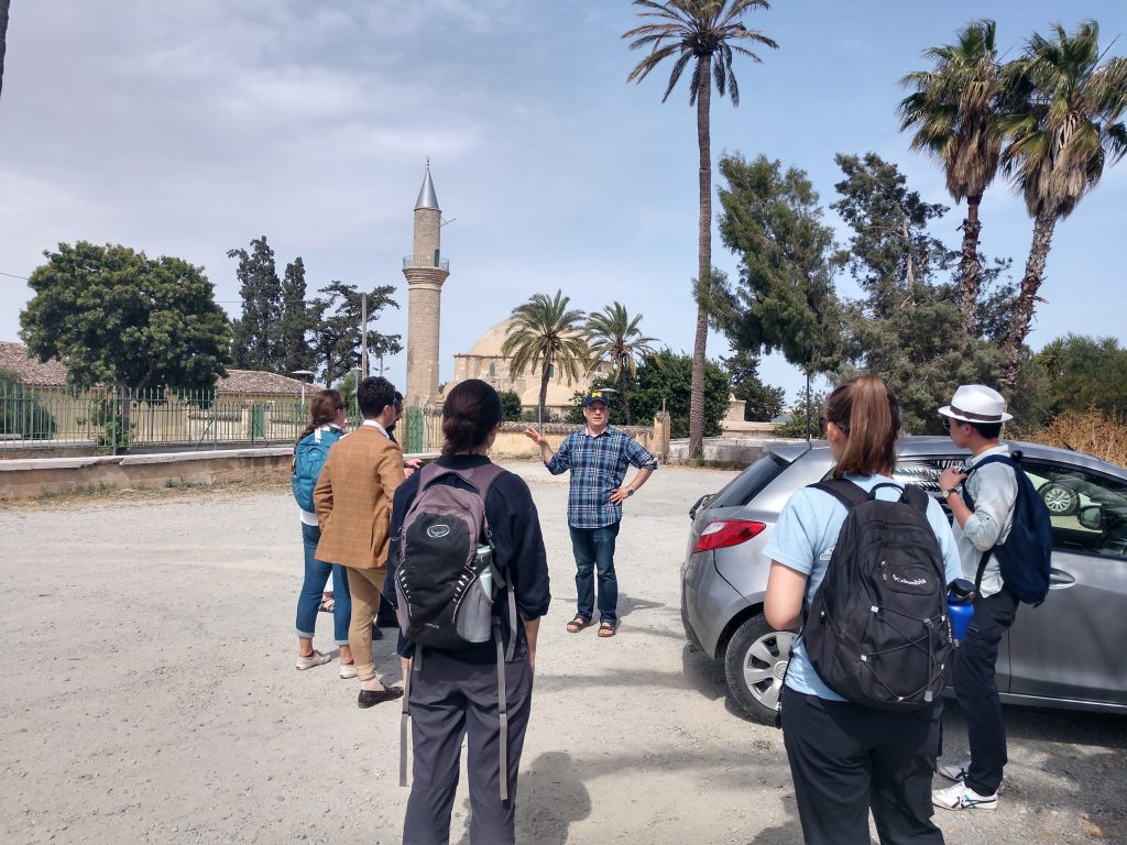 The group stands in a dirt parking lot with palm trees and a minaret in the distance near background