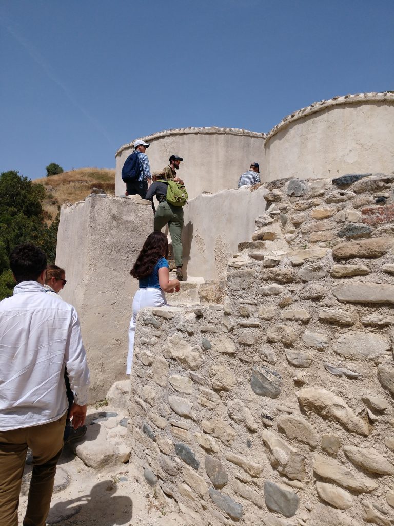 A line of people climb a short set of steps in a wall toward small, round, white buildings.