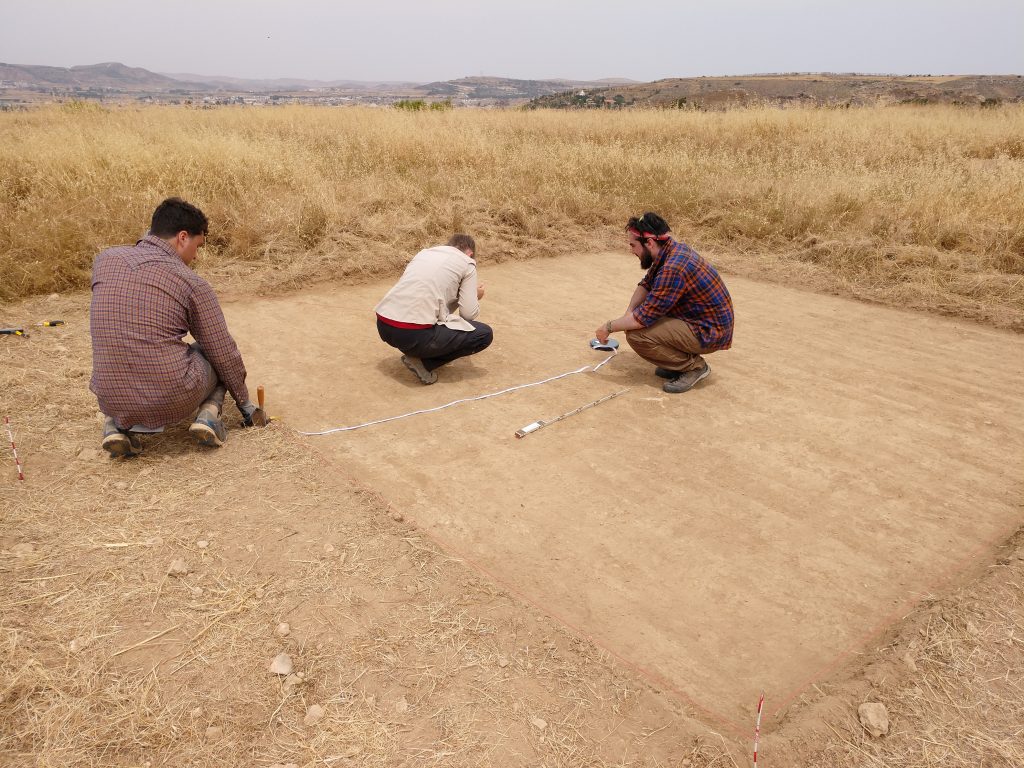 Three people measure an archaeological trench with exposed plow marks