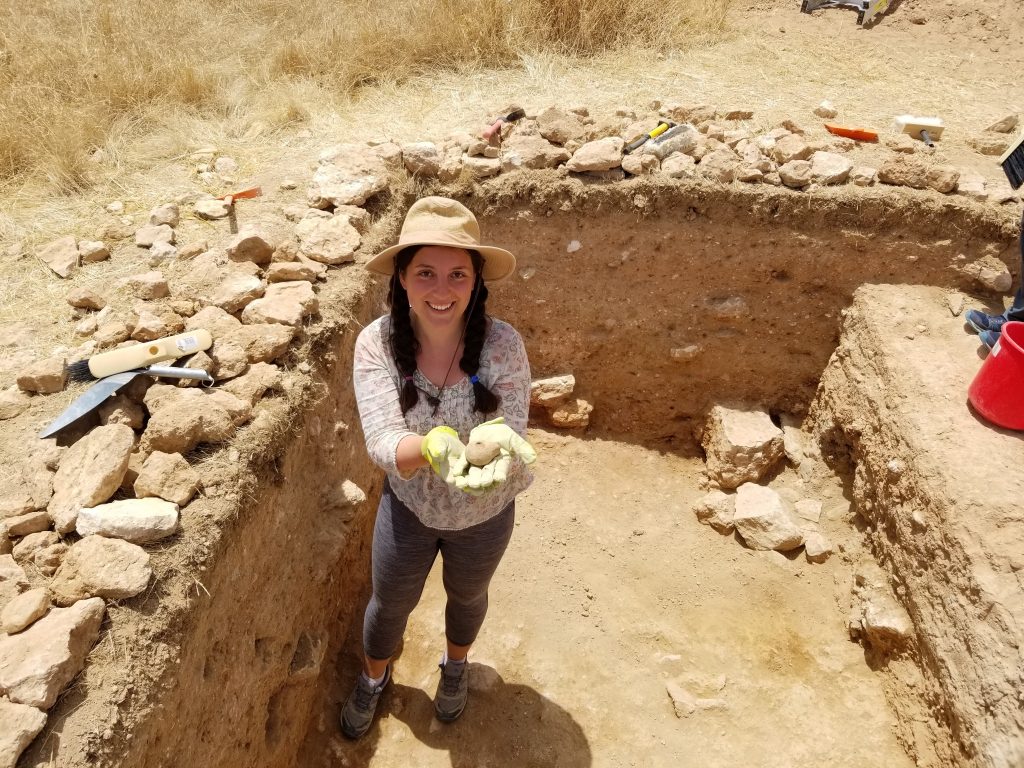 A happy archaeologist holds a small ceramic lamp