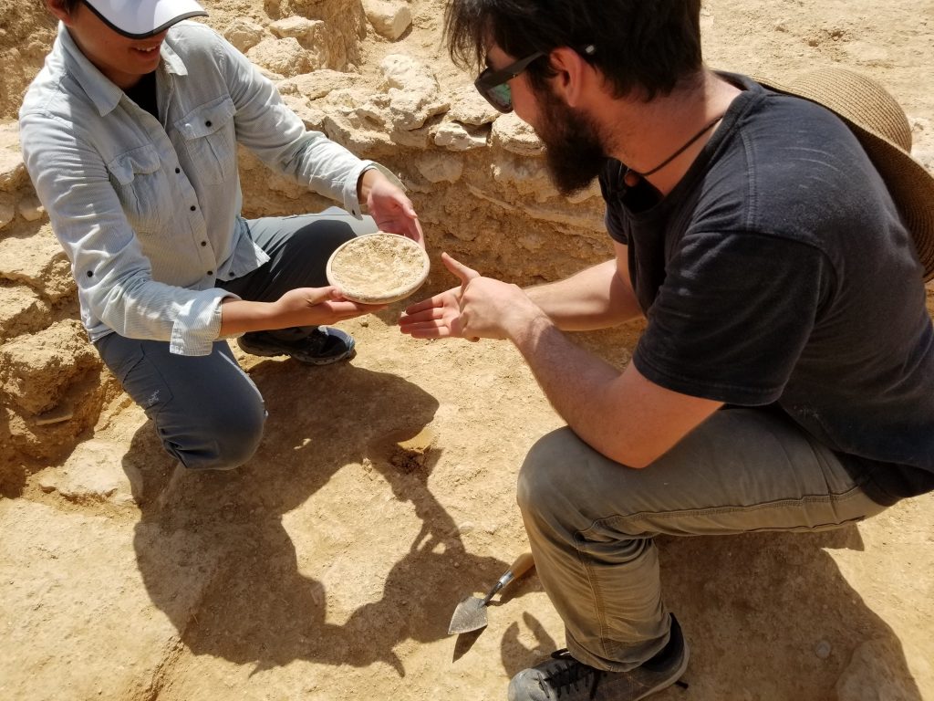 Two archaeologists carefully remove an intact bowl