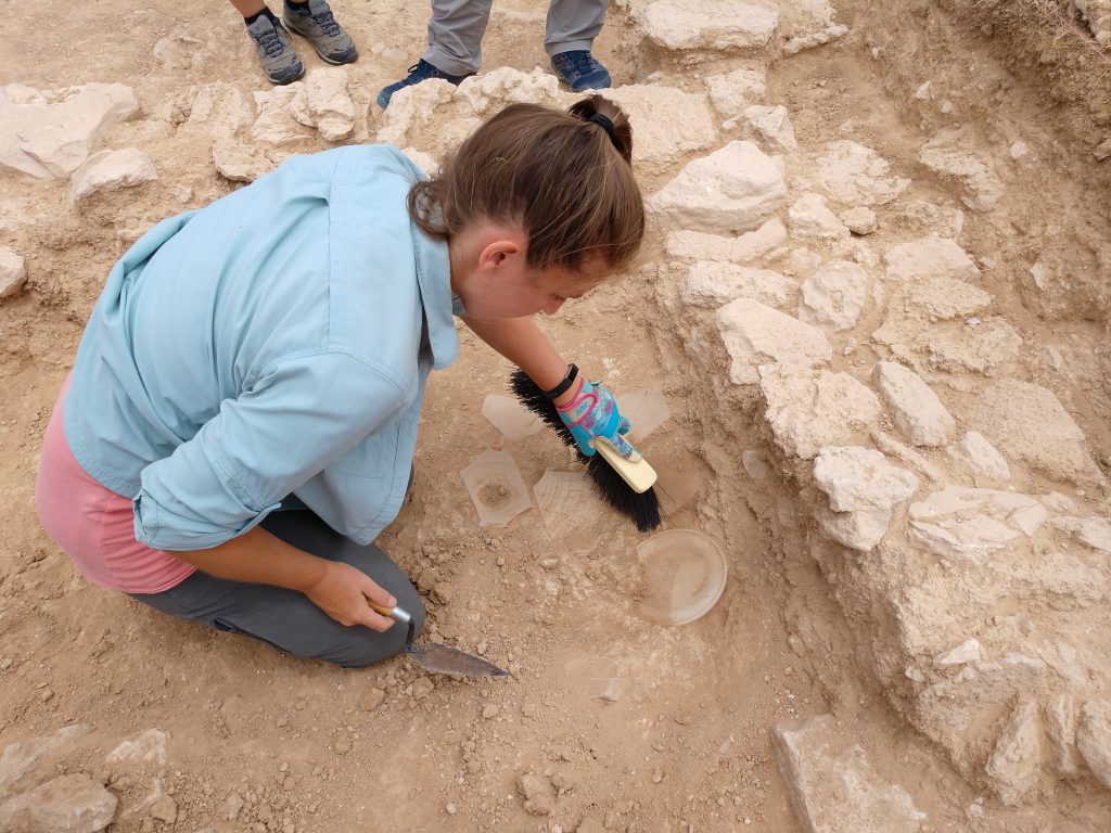 An archaeologist brushes dirt from a circular pot lid