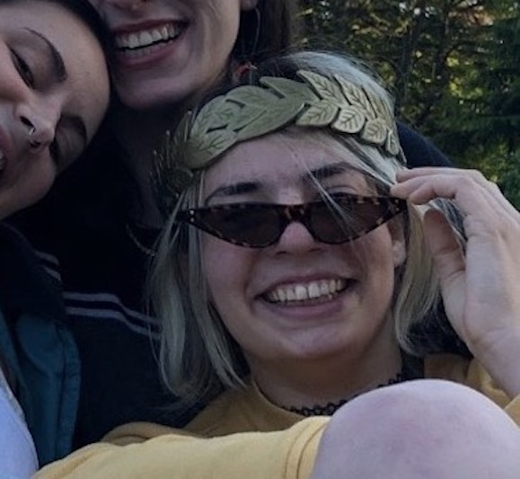 Mitzi with friends, wearing plastic laurels and stylized sunglasses, smiling.
