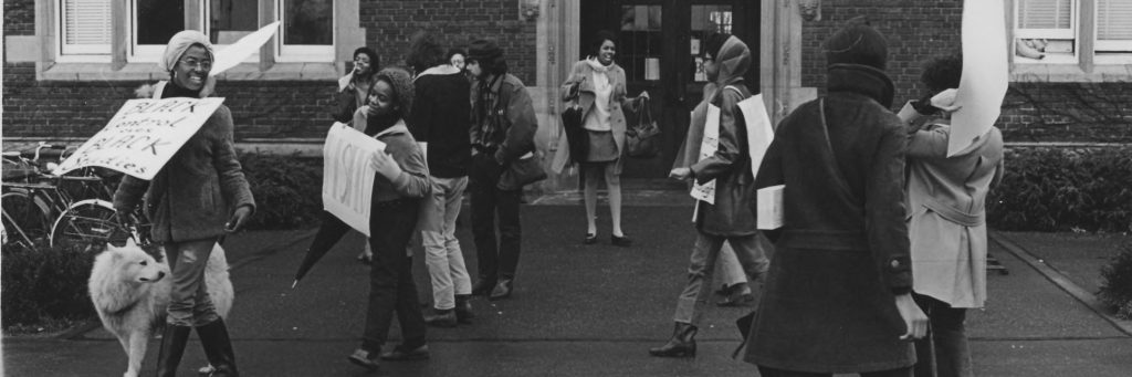 Black and white photograph of Reed students protesting outside of Eliot Hall with signs. The photograph is the same as used in the event flyer.