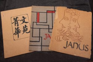 Photograph of three fanned out publications titled Janus. The publication's cover on the left is mostly plain with blue characters written on the front. The publication's cover in the middle is light blue with angled navy blue lines and occasional red boxes. The publication's cover on the right is a depiction of a two-faced person with a beard, assumed to be an image of the roman god Janus.