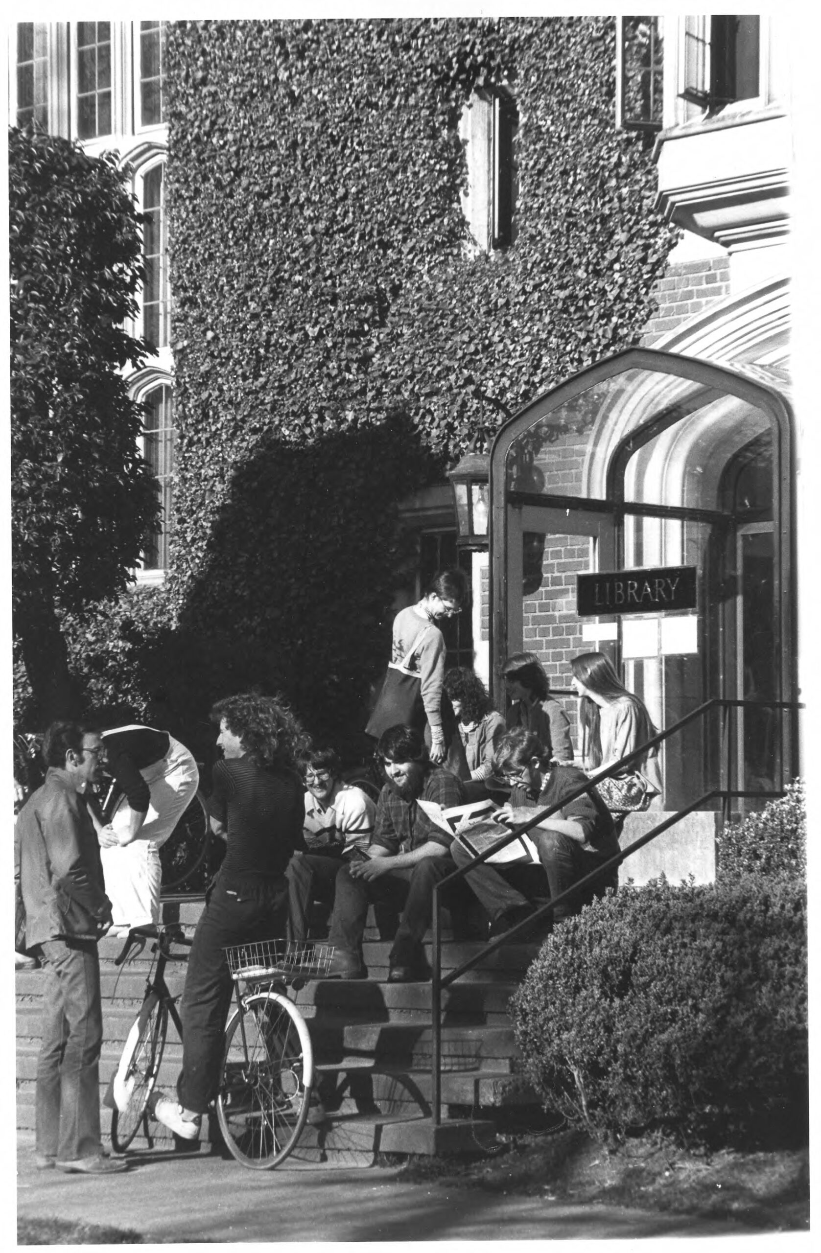 Students sitting on the front steps of the ivy-covered Hauser Memorial Library, circa 1977.