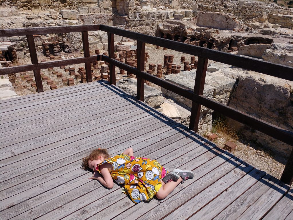 A small child lays down on a boardwalk overlooking the ruins of a bath complex
